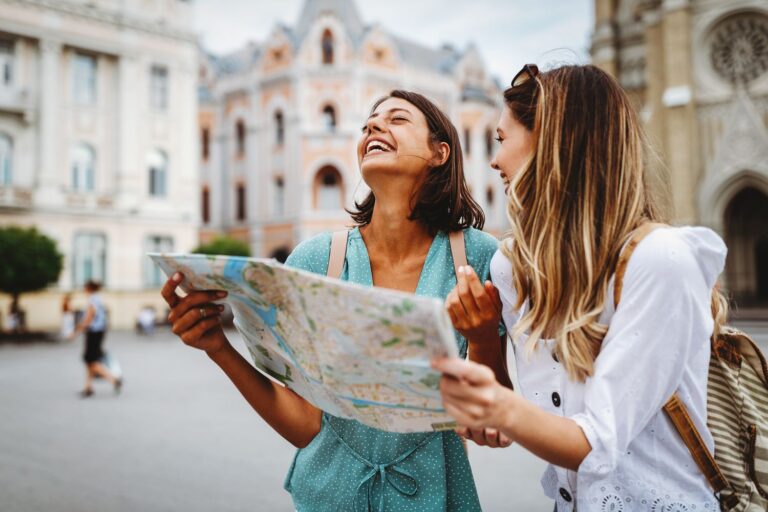 Fun, friends, travel and tourism concept. Beautiful happy women looking for direction in the city